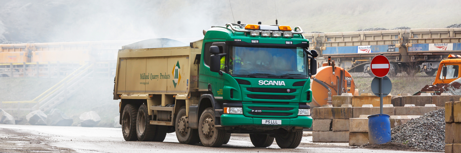 MQP truck driving through an asphalt plant site with train in the background.
