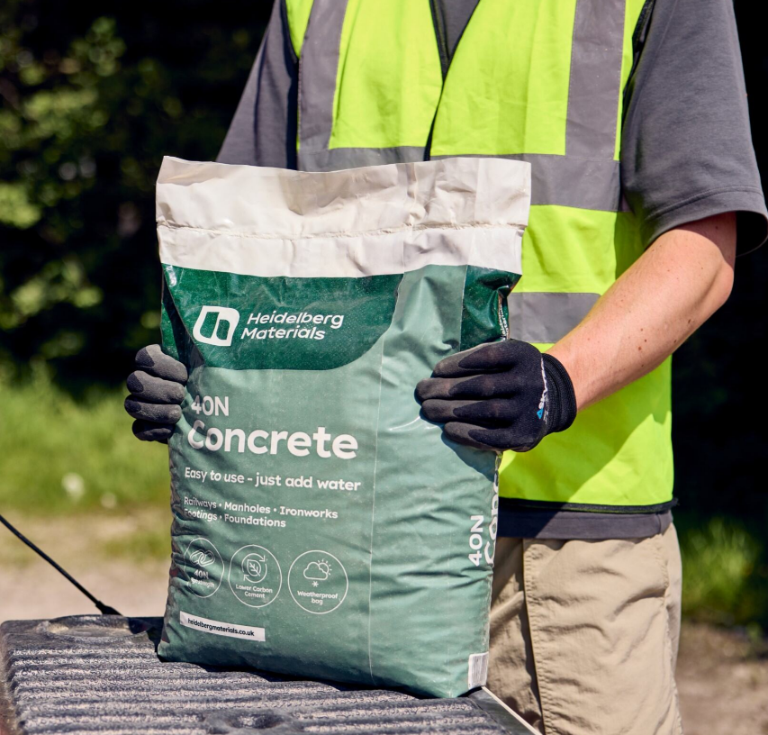 A person in a safety vest holding a Heidelberg Materials bag of concrete.