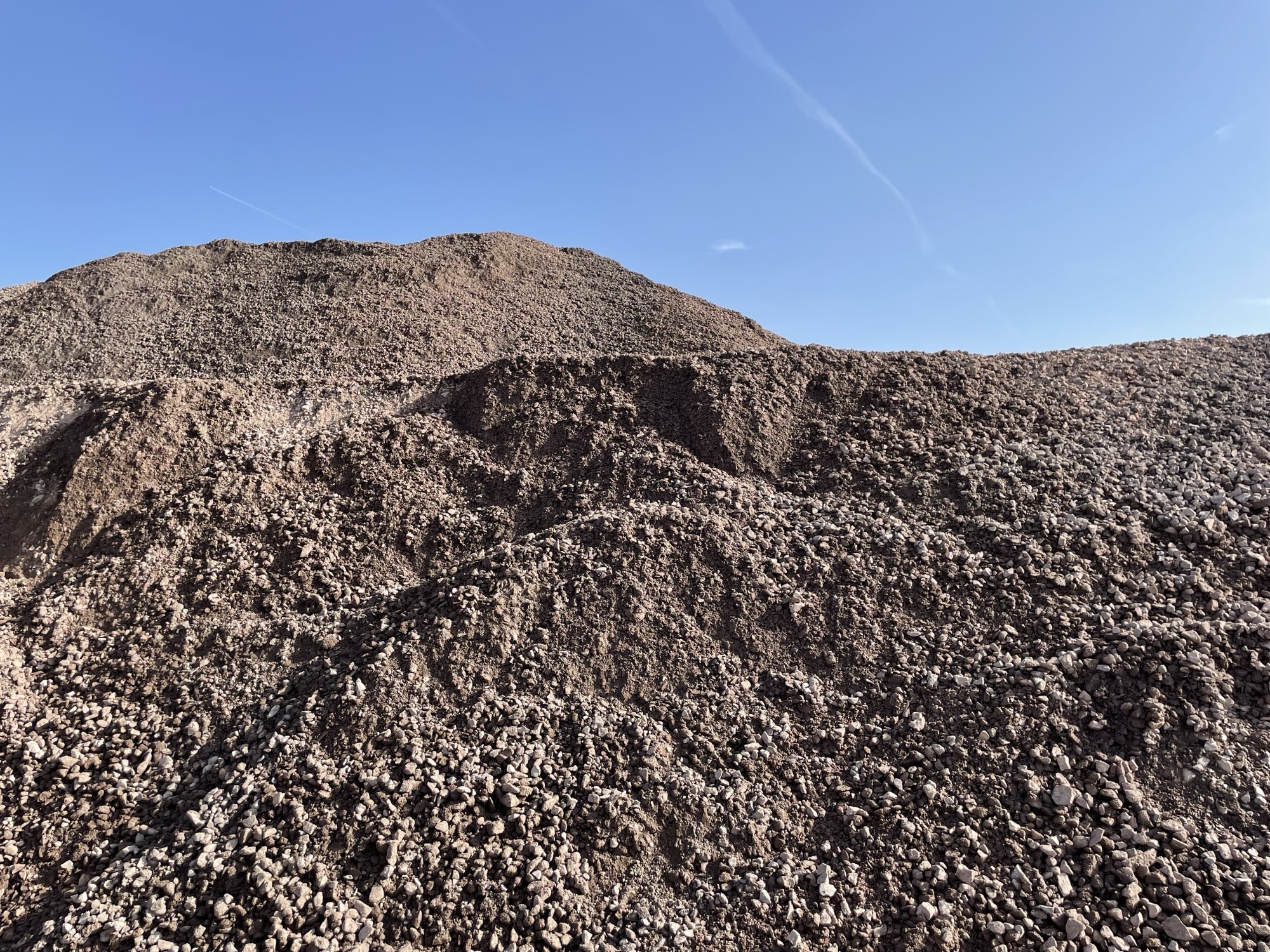 A large pile of gravel under a clear blue sky at an industrial site.