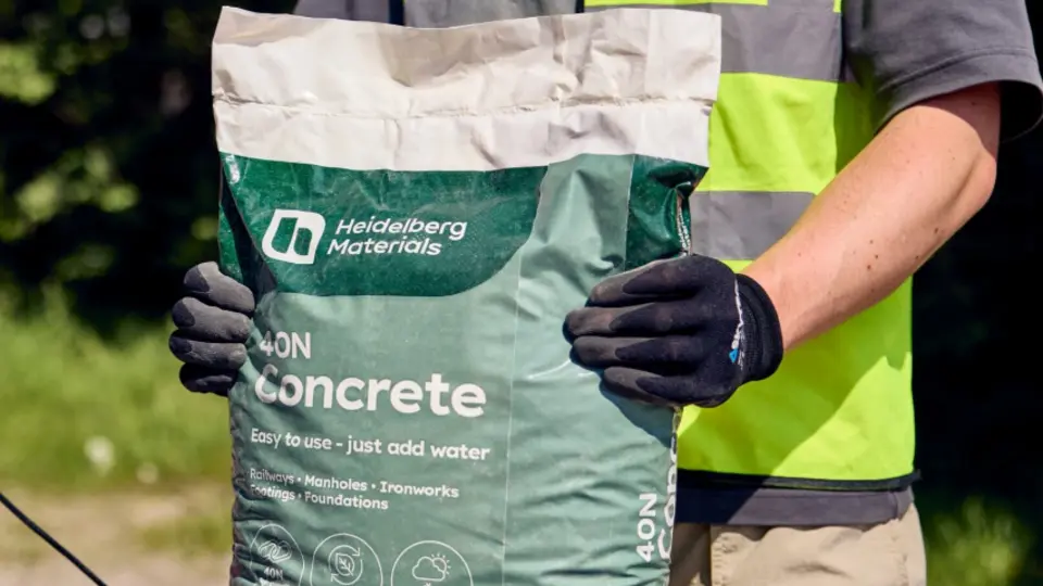 A person in a safety vest holding a Heidelberg Materials bag of concrete.