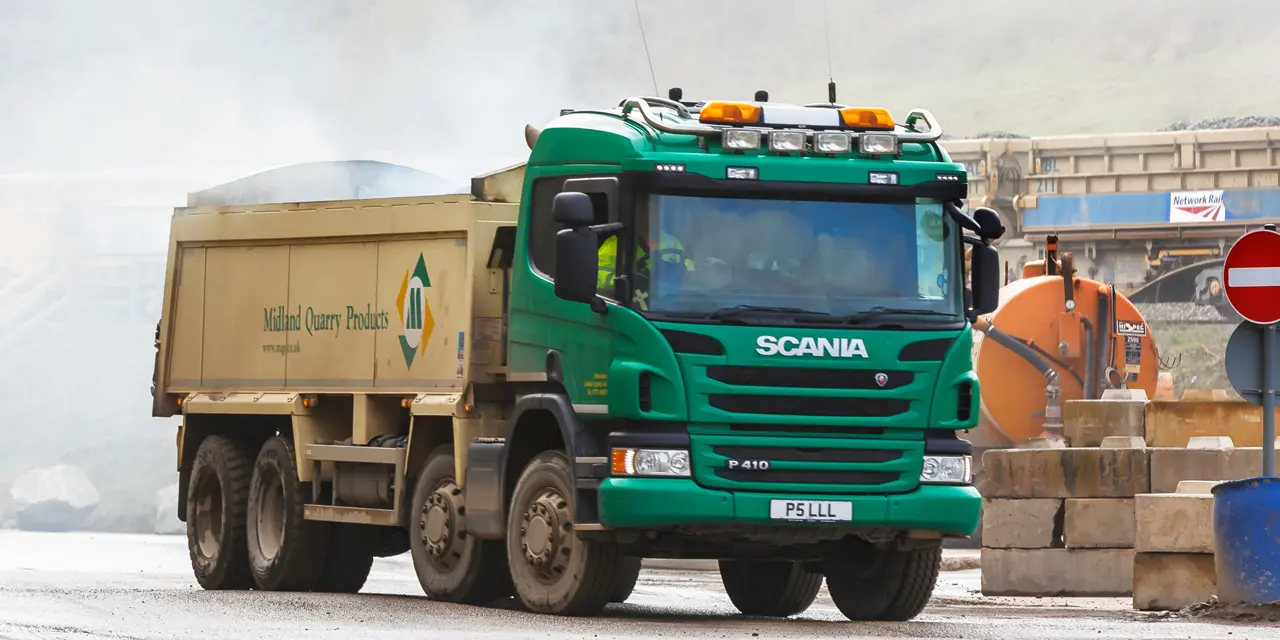 MQP truck driving through an asphalt plant site with train in the background.