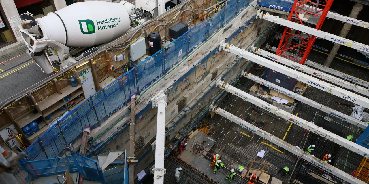 A construction site with workers, scaffolding, and a Heidelberg Materials ready-mixed concrete truck in the background.
