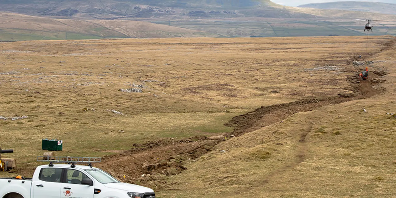 A helicopter drops aggregate onto the Sulber Nick path on Ingleborough, with Penyghent in the distance